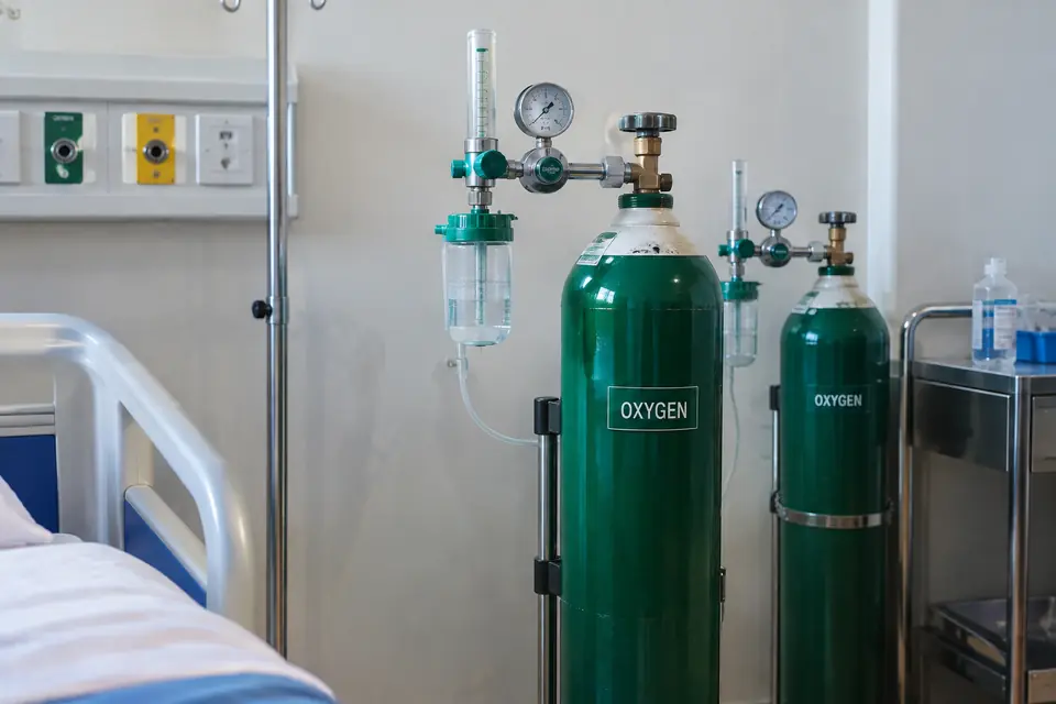 Two green oxygen cylinders with flowmeters and humidifier bottles beside a hospital bed